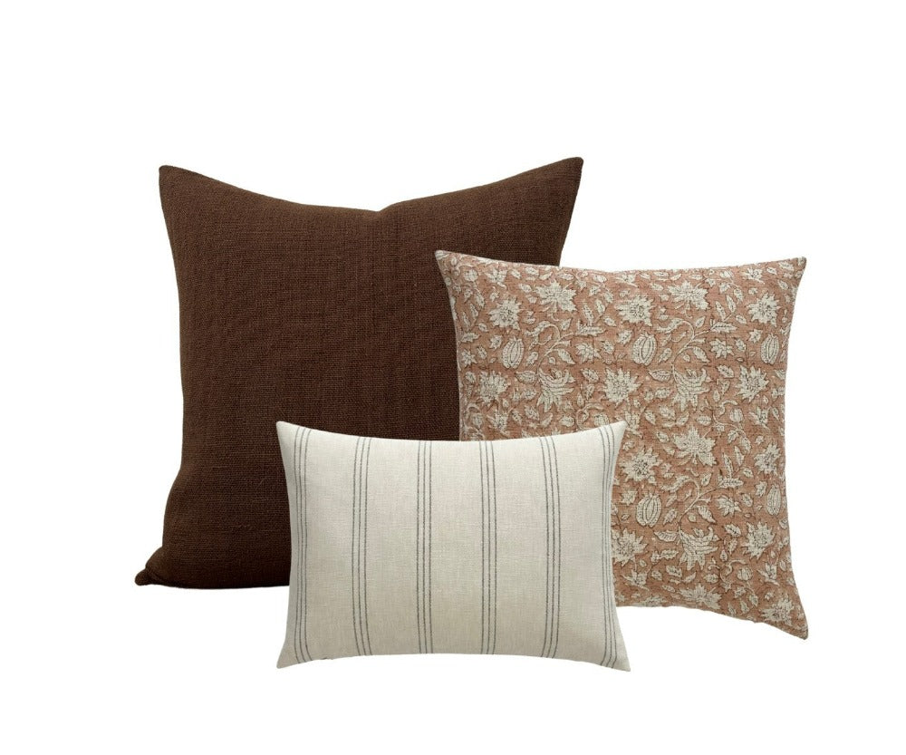 A collection of 3 pillow covers of different size and pattern. A large solid brown pillow in the background, a block printed pillow with a coral color and an off white lumbar in front.