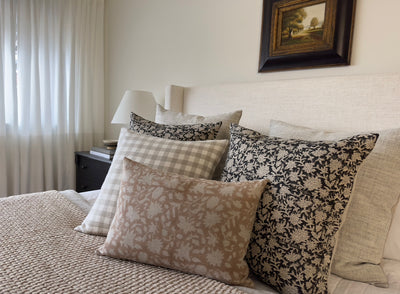 A bed with 6 throw pillows in 4 different patterns and colors. Landscape painting with wide black frame hangs above the bed.
