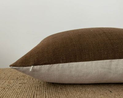 A hand woven brown pillow cover with the zipper pull of a hidden zipper. 